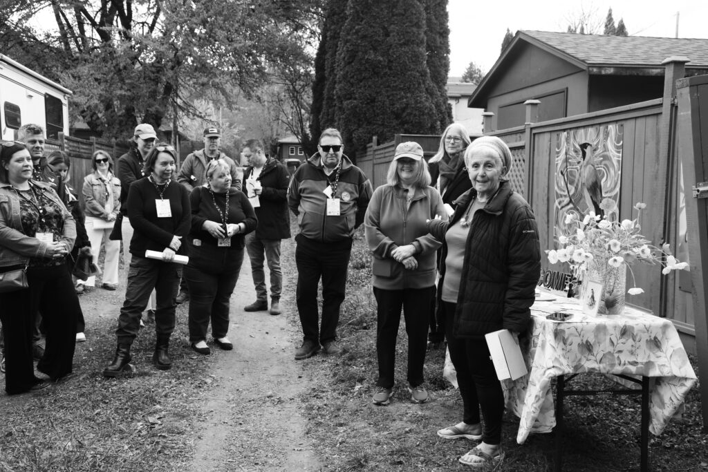 Black and white photo of 13 people standing in a laneway discussing laneway beautification